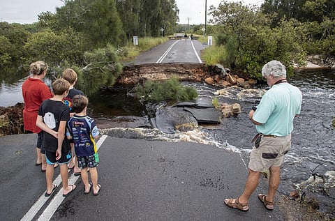 People stand at a washed out section of road at Port Stephens, 200 kilometers north of Sydney, Australia. People across New South Wales have been warned to expect intense rain and potentially life-threatening flooding, with Sydney predicted to be deluged with up to 200 millimeters of rain in one day. (Photo | AP)