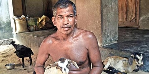 Kanhu Rout sits with a baby goat at his house.