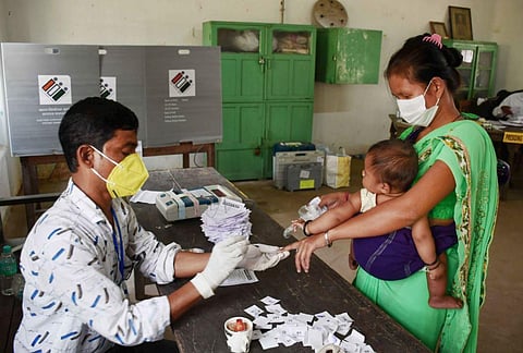 A poll official marks the finger of a voter with indelible ink as she arrives to cast her vote during the first phase of polling for Assam Assembly elections, at Koliabor in Nagaon district. (Photo |