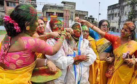 Women, wearing PPE kit, play with dry colours during the Holi festival, as coronavirus cases spike across the country, at Begumbazar in Kolkata. (Photo | PTI)