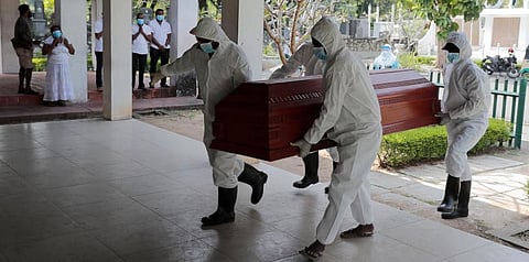 Sri Lankan health workers carry a coffin carrying remains of a COVID -19 victim to a cremation furnace as relatives watch from a distance in Colombo. (Photo | PTI)