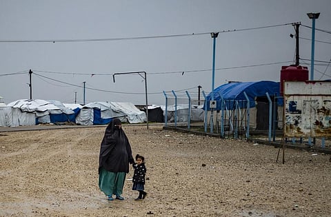 A woman holds a child's hand as they stand in the rain at Camp Roj, where relatives of people suspected of belonging to IS are held, in Syria. (Photo | AFP)