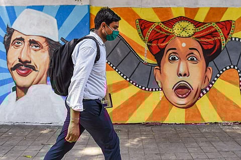 A man wearing a face mask as a precaution against Covid-19 walks past a mural at Lalbaug in Mumbai. (Photo | PTI)