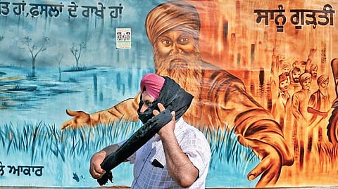 A man walks in front of a graffiti at the Ghazipur border during the ongoing farmers’ agitation on Friday. Saturday marks the 100th day of the sit-in protest at Delhi borders | Pti