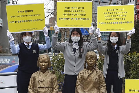 High school students hold up banners to protest a recent academic paper by Harvard University professor J. Mark Ramseyer, behind statues symbolizing wartime sex slaves in Seoul. (Photo | AP)