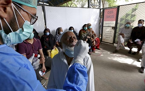 An elderly man reacts while having a nasal swab sample taken by a health worker while others wait their turn at a COVID-19 testing facility in a hospital in Karachi (Photo | AP)