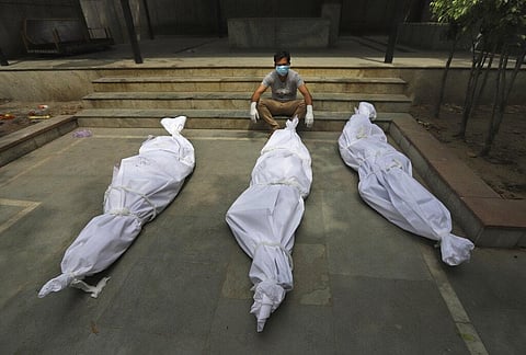 A man waits for the cremation of a relative who died of COVID-19, placed near bodies of other victims, in New Delhi, India. (Photo | AP)