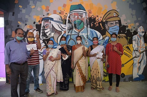Voters in Assam pose at a polling booth, in front of wall art dedicated to COVID warriors. (Photo | Special Arrangement)