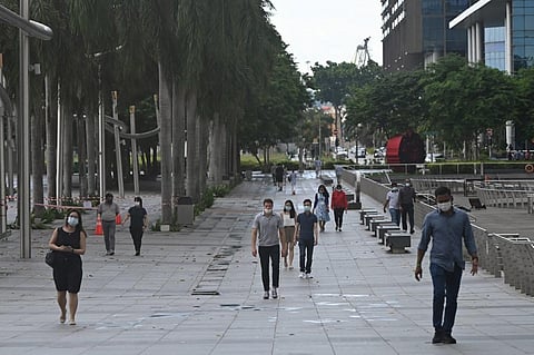 People wearing face masks walk along the promenade at Marina Bay in Singapore on May 14, 2021. (Photo | AFP)