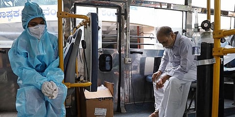 A health worker keeps a check on a COVID-19 patient recieving oxygen in a bus, in Bengaluru, Saturday. (Photo | PTI)