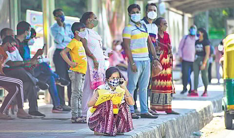 People, wearing face masks, wait for buses near Safdarjung Hospital on Thursday | PTI
