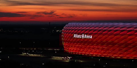 The sun sets behind the illuminated 'Allianz Arena' soccer stadium in Munich, Germany. (Photo | AP)