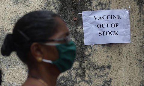 A woman wearing mask walks past a notice about the shortage of coronavirus vaccine supply outside a vaccination centre. (File Photo | AP)