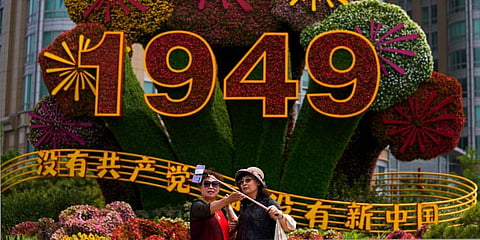 Chinese women take a selfie with a floral decoration carrying the words 'Without the Communist Party, There would be no new China' setup in Beijing, June 28, 2021. (Photo | AP)