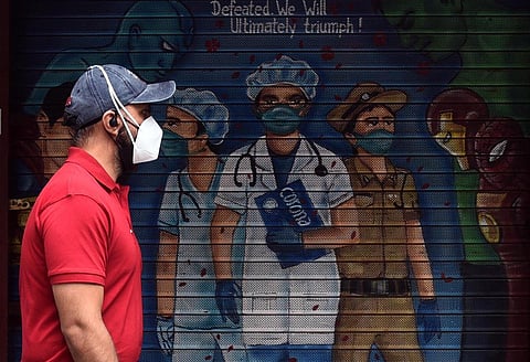 A man walks past a mural on COVID-19 warriors, painted on the shutter of a shop, during the Covid-induced lockdown. (Photo | Parveen Negi, EPS)