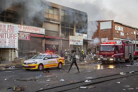 A woman walks past a fire truck as it extinguishes flames in a looted store in Alexandra township, Johannesburg, South Africa. (Photo | AP)