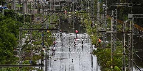 Commuters walk on waterlogged railway tracks following heavy rains, at Kurla in Mumbai, Sunday, July 18, 2021. (Photo | PTI)