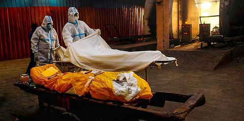 A relative along with a health worker helps to place the body of a person who died from COVID-19 before cremation. (File Photo| PTI)