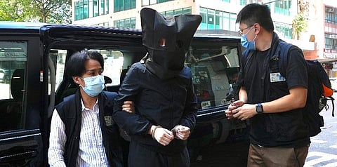 A hooded suspect is accompanied by police officers to search evidence at office in Hong Kong Thursday, July 22, 2021. (Photo | AP)