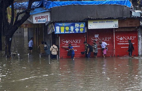 People make their way through a waterlogged street after heavy rainfall in Mumbai. (Photo | AP)