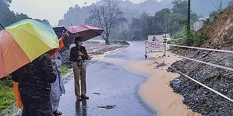 A policewoman holding umbrella, inspects a damaged roadside during rain. (Photo | PTI)