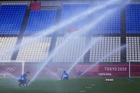 Grounds crew members spray the field down with water before the start of a men's soccer match between New Zealand and Honduras at the 2020 Summer Olympics. (Photo | AP)
