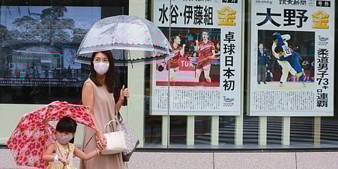 People wearing face masks to protect against the spread of the coronavirus walk past extra papers reporting on Japanese gold medalists at Tokyo Olympics. (Photo| AP)