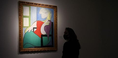 A gallery worker poses alongside an artwork titled 'Femme assise près d'une fenêtre (Marie-Thérèse)' by Pablo Picasso during a photocall at Christie’s auction house in London. (Representation | AFP)