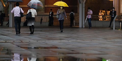 People wearing face masks walk by a train station in the rain in Tokyo. (Photo | AP)
