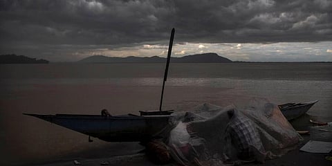 Fishermen take shelter from the rain under a plastic sheet as monsoon clouds hover over the river Brahmaputra. (Photo | AP)