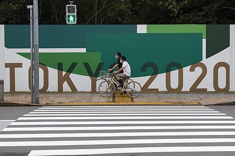Men wearing face masks ride bicycles along the wall installed to close off a park being prepared for the Olympics and Paralympics Games in Tokyo. (Photo | AP)
