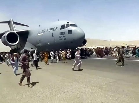 Hundreds of people run alongside a U.S. Air Force C-17 transport plane as it moves down a runway of the international airport, in Kabul. (Photo | AP)