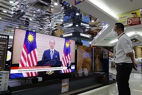 An electronic shop staff wearing a face mask watches live broadcast of Malaysian Prime Minister Muhyiddin Yassin speak at a shopping outlet in Kuala Lumpur. (Photo | AP)