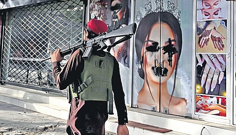 A Taliban fighter walks past a beauty salon with images of women defaced using spray paint in Kabul on Wednesday | AFP