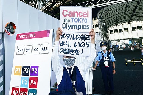 One of the anti-Olympic protesters gathered outside Ariake Tennis Park holds placards at the 2020 Summer Olympics in Tokyo. (Photo | AP)