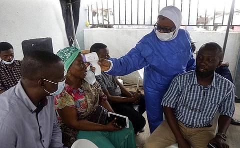A nurse in protective gear, center, takes temperature of people waiting to take the Moderna coronavirus vaccine. (Photo | AP)