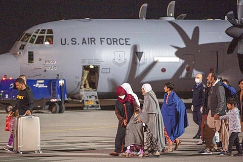 Families evacuated from Kabul, Afghanistan, walks past an U.S air force airplane that flew them at Kosovo's capital Pristina International Airport. (Photo | AP)