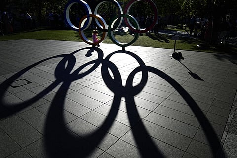 A child sits in the Olympic rings on display outside the Olympic Stadium where the athletic events are underway at the 2020 Summer Olympics. (Photo | AP)