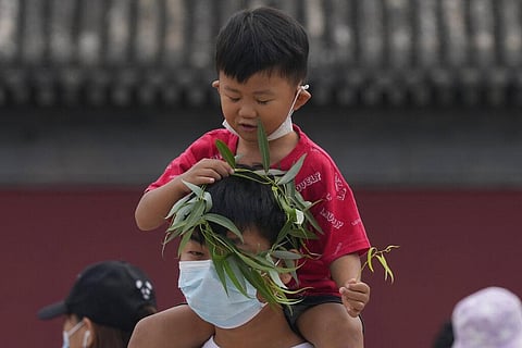 A child puts a wreath over the head of a man wearing a mask in Beijing. (Photo | AP)