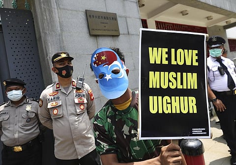 A Muslim student wearing a mask with the colors of the pro-independence East Turkistan flag, and the China's flag in the shape of a hand holds a poster outside Chinese Embassy in Jakarta. (Photo | AP)