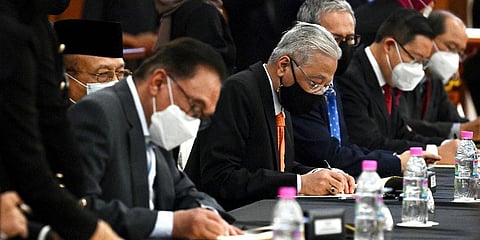 Malaysian Prime Minister Ismail Sabri Yaakob, center, and opposition leader Anwar Ibrahim, left, sign documents during a ceremony at Parliament in Kuala Lumpur, Malaysia, Sept 13, 2021. (Photo | AP)