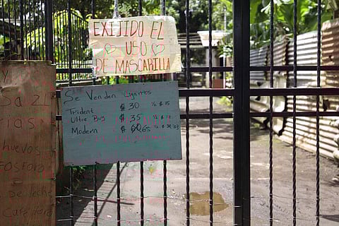 A sign requiring the use of masks during the COVID-19 pandemic hangs over signs advertising cigarettes, eggs, matches, milk and coffee for sale on a gate at the entrance. (Photo | AP)