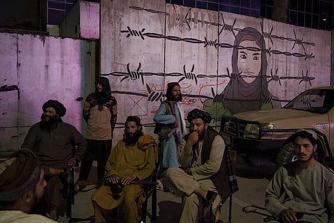 Taliban members sit in front of a mural depicting a woman behind barbed wire in Kabul, Afghanistan. (Photo | AP)