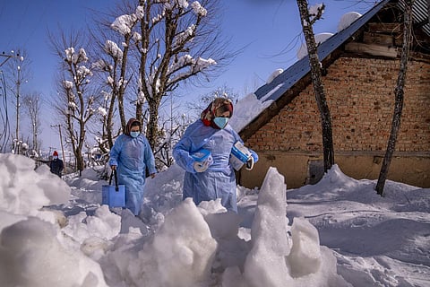 Fozia, right and Tasleema, Kashmiri healthcare workers, carry vaccines as they walk on a snow covered road during a COVID-19 vaccination drive in Budgam, southwest of Srinagar. (Photo | AP)
