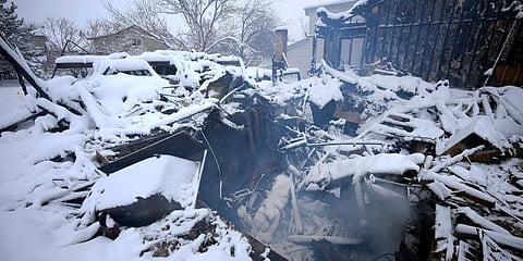 A lone flame flickers as smoke roils from the remains of a home destroyed by a pair of wildfires in Superior, Colorado. (Photo | AP)