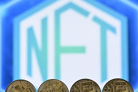 An illustration picture taken in London on December 30, 2021, shows gold plated souvenir cryptocurrency coins arranged by a screen displaying a NFT (Non-Fungible Token) logo. (Photo | AFP)