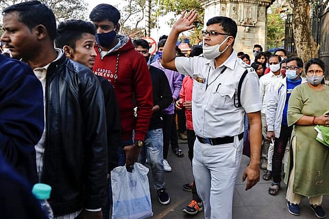 A policeman, wearing a face mask around his chin, reprimands a youngster for not wearing a face mask as people line up to enter a park on New Year's Day in Kolkata. (Photo | AP)