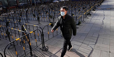 A resident wearing a mask to help protect from the coronavirus walks past barricades and tents prepared for mass testing at a neighborhood in Beijing. (Photo| AP)