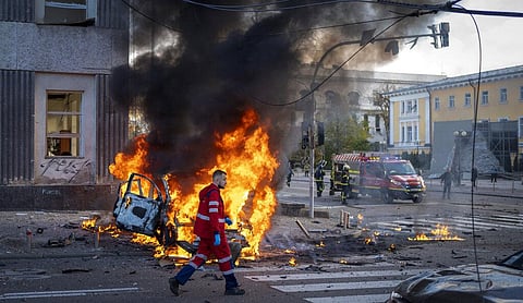 A medical worker runs past a burning car after a Russian attack in Kyiv, Ukraine on October 10, 2022. (Photo | AP)