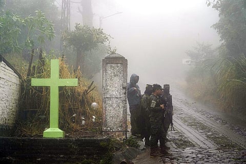 Soldiers stand guard under the rain near a cross that decorates a road in Comasagua, El Salvador on October 10, 2022. (Photo | AP)